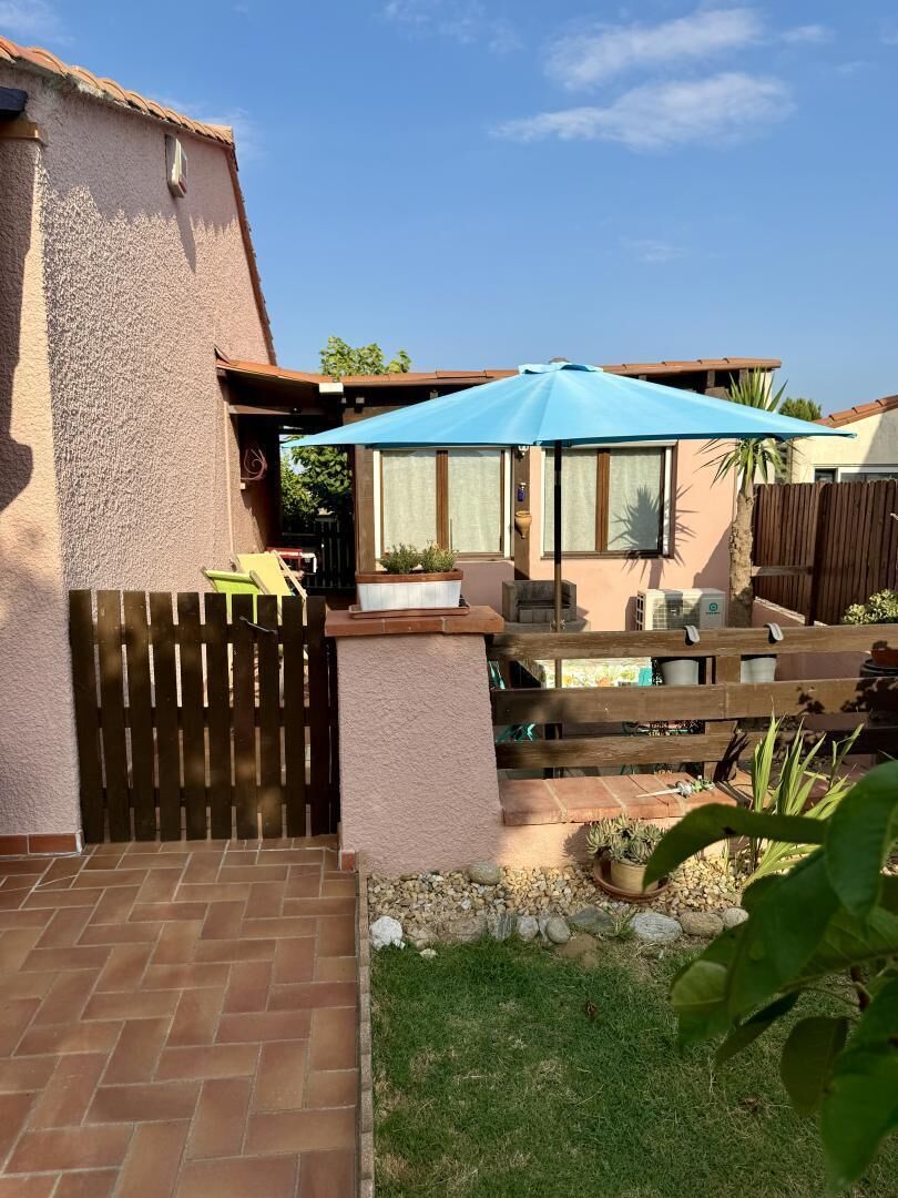 Un patio con cerramiento de madera, una sombrilla azul y mobiliario exterior.