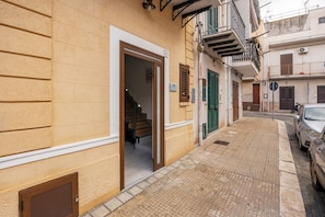 A narrow street with a building entrance, a staircase, and a parked car.