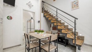 A dining area with a table and chairs, a staircase with wooden steps and metal railings, and a wall-mounted television. - Casa Lucid'amare Relaxation with Private Terrace, Wi-Fi & Air Conditioning (isola delle femmine)