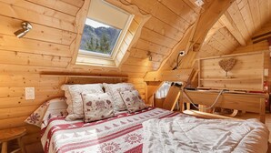 A cozy wooden cabin bedroom with a bed, pillows, a desk, and a skylight.