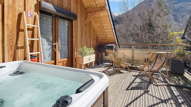A wooden cabin with a hot tub, a ladder, a barbecue, and a view of mountains.
