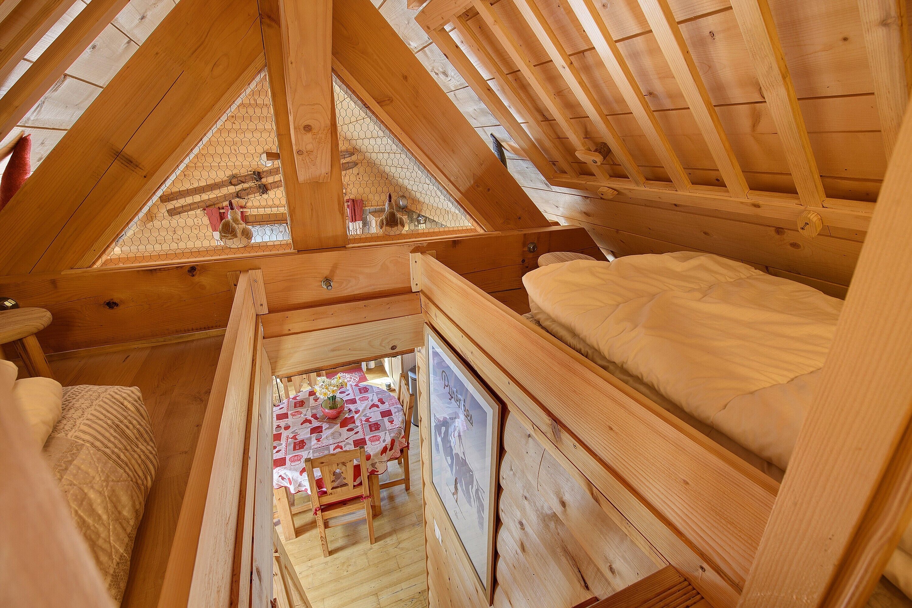 Une chambre mansardée en bois, avec un plafond en pente, une petite table à manger avec des chaises et un tableau encadré accroché au mur.