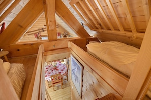 Ein Schlafzimmer im Mansardenstil mit Holzbalken, einem kleinen Esstisch mit Stühlen und einem gerahmten Bild an der Wand.