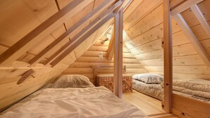 A wooden interior with a sloped ceiling, a bed with white bedding, and a small bedside table.