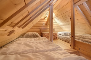 A wooden interior with a sloped ceiling, a bed with white bedding, and a small bedside table.
