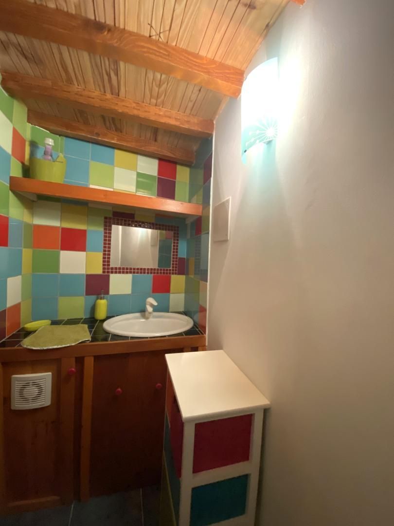 Un bany petit amb sostre de fusta, rajoles quadriculades i de colors, un lavabo blanc i un petit armari.