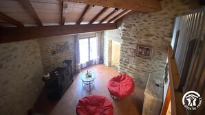 Un intérieur rustique avec des poutres apparentes, des murs en pierre et un coin salon confortable agrémenté de fauteuils en forme de haricots rouges.