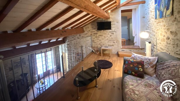 Une chambre de style loft rustique, avec des poutres en bois apparentes, un mur en pierre, un lit agrémenté d’oreillers à motifs, une petite table et un téléviseur fixé au mur.