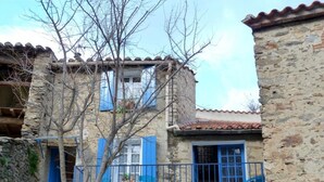 Un bâtiment en pierre avec des volets bleus et un balcon agrémenté d’une table et de chaises.