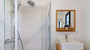 Een badkamer met een douchecabine van glas, een witte wastafel en een houten wastafelmeubel.