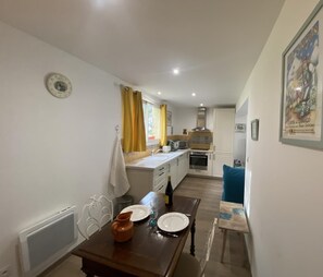 A compact kitchen with white cabinets, a stove, and a microwave. There is a dining table with plates and a pitcher.