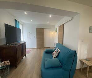 A living room with a sofa, a TV on a wooden cabinet, and a small table.