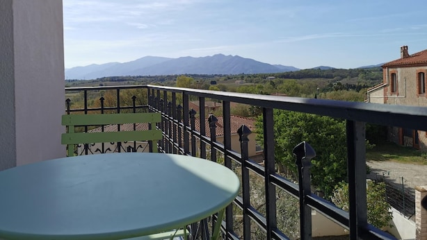 Ein Balkon mit Tisch und Blick auf Berge und Gebäude.
