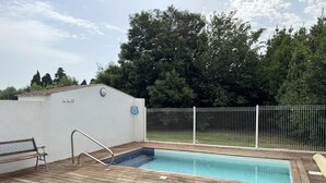 A wooden deck with a swimming pool, a bench, and a white wall with a door. - Illibéris 2 gardens (ELNE)