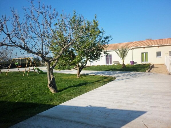 A residential area with a paved driveway, a swing set, and a house with a tiled roof. - Illibéris 2 gardens (ELNE)