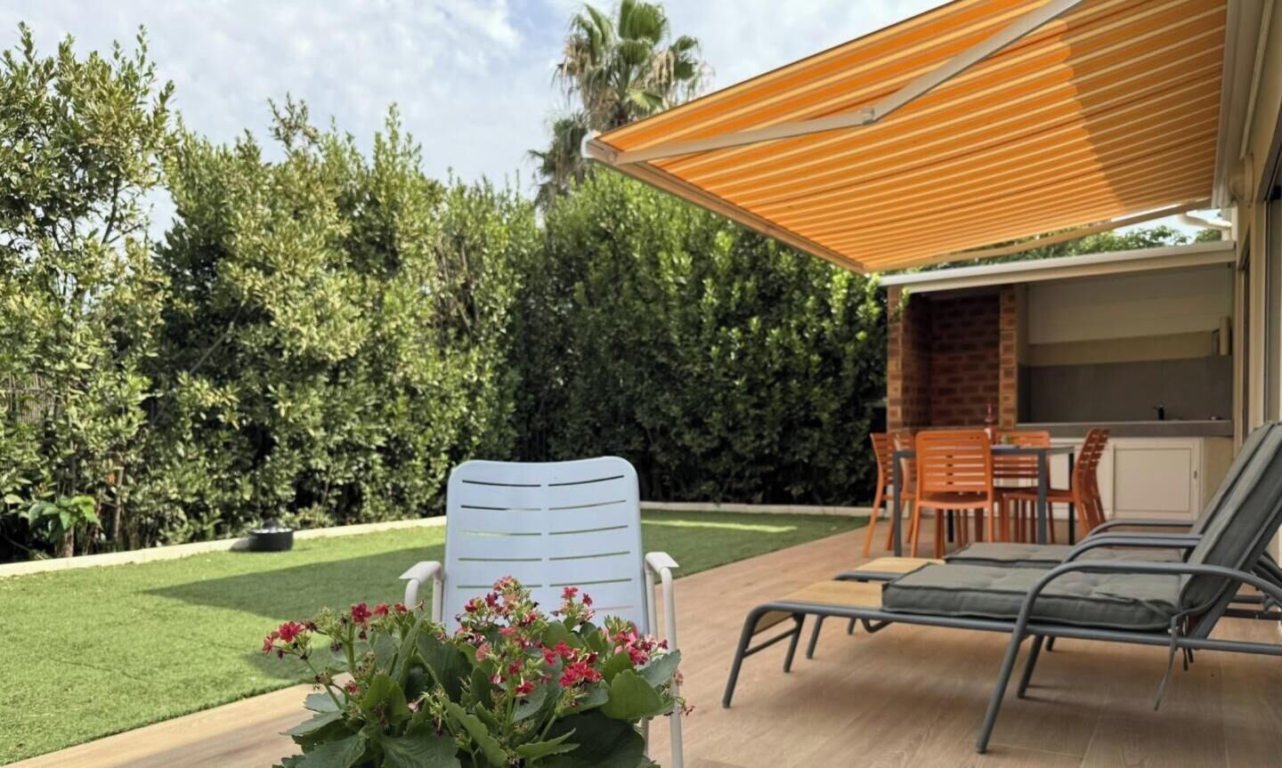 Eine Terrasseneinrichtung im Freien mit Esstisch und Stühlen, einer Liege und einem Blumentopf mit Blumen.