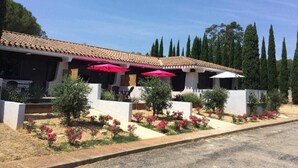 A building with a tiled roof, outdoor seating with red umbrellas, and a landscaped garden with pink flowers. - Carène - ARGELES-SUR-MER (ARGELES-SUR-MER)