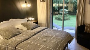 A bedroom with a large bed, a nightstand with a lamp, and a view of a garden through a sliding door. - Les melias - ST-FELIU-D'AVALL (ST-FELIU-D'AVALL)