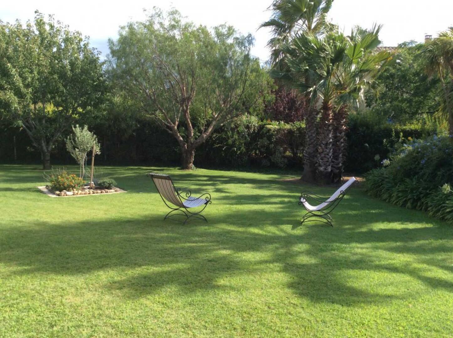 A well-maintained lawn with two outdoor chairs and a variety of trees and shrubs.