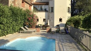 Un área de piscina con una pileta rectangular, sillas de descanso y una cerca de madera.