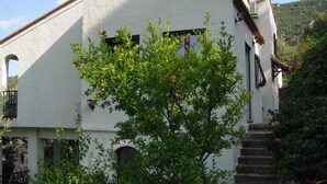 Un edificio bianco con tetto spiovente, una scala che conduce a una porta e un albero in primo piano.