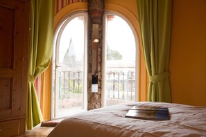 A room with a bed, a window with a view of a balcony, and curtains.