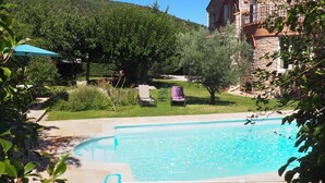 Un espace piscine avec un bâtiment en pierre en arrière-plan, entouré de verdure.