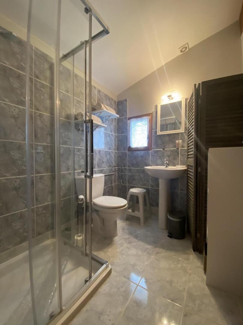 Een badkamer met een glazen douchecabine, toilet, wastafel en spiegel.