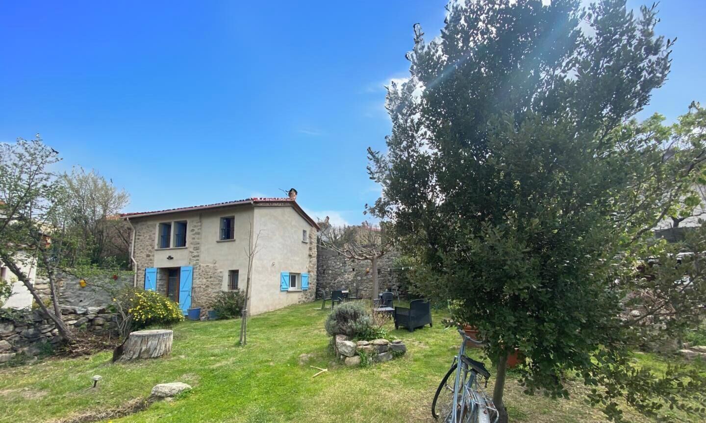 Une maison en pierre avec des volets bleus, un vélo et un jardin bien entretenu.