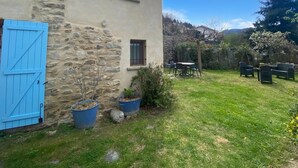 Ein Steinhaus mit blauer Tür, einem kleinen Fenster und einer Terrasse mit Gartenmöbeln.