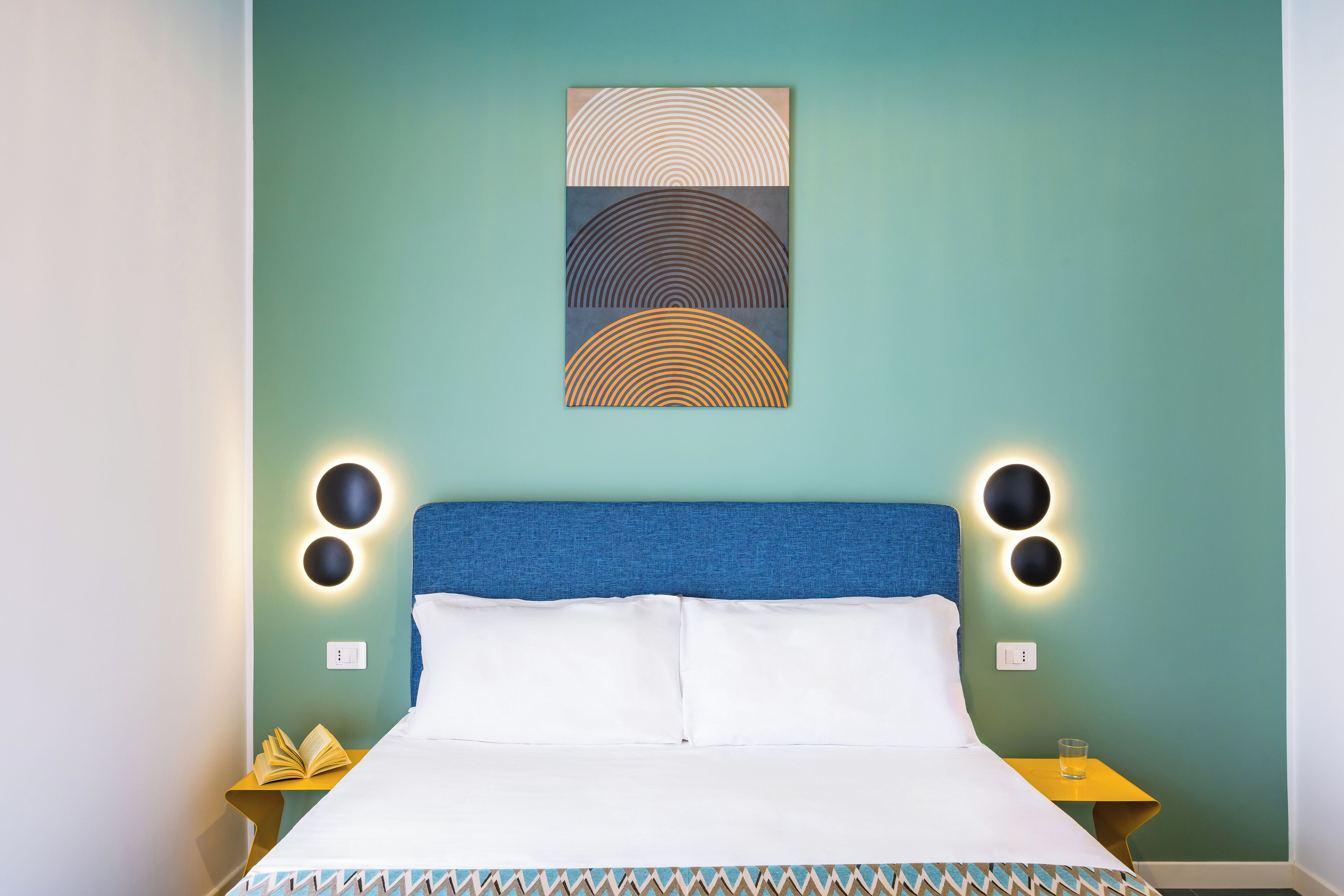 A neatly made bed with a blue headboard, two bedside tables with lamps, and a wall art piece above the bed.