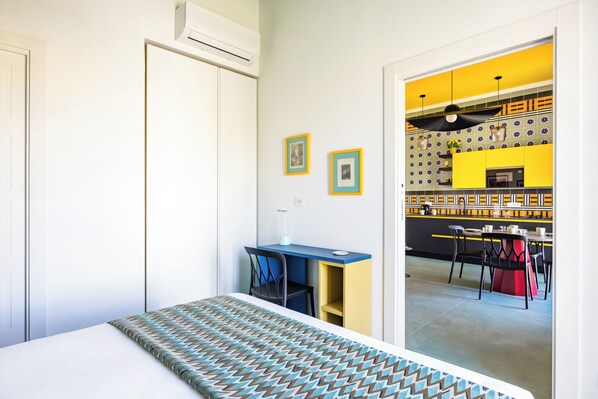 Une chambre avec un lit, un bureau et une chaise. Il y a une porte et un appareil de climatisation sur le mur.