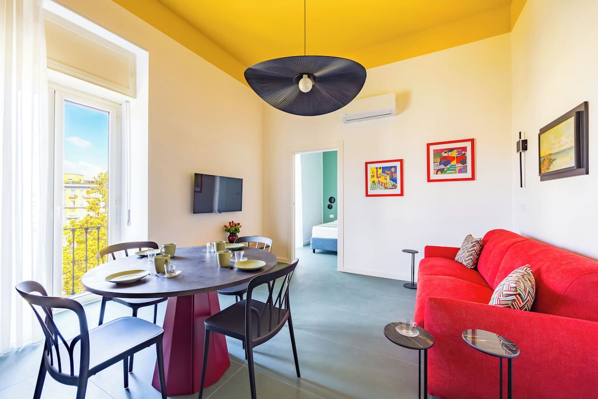 A modern living room with a red sofa, dining table with chairs, and artwork on the walls.