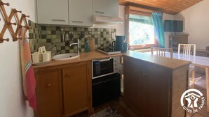 A compact kitchen with wooden cabinets, a sink, a stove, and a window with a view of greenery.