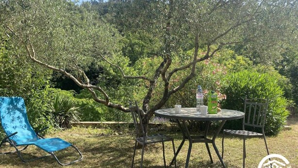 An outdoor seating area with a table and chairs, surrounded by greenery and trees.