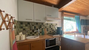 A compact kitchen with wooden cabinets, a sink, a stove, and a window with a view of greenery.