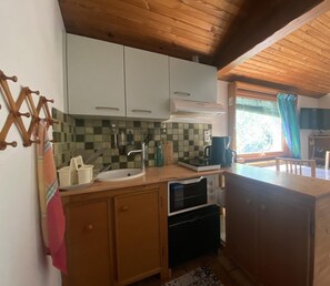 A compact kitchen with wooden cabinets, a sink, a stove, and a window with a view of greenery.