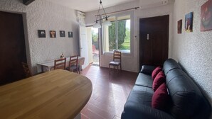 Un comedor con mesa y sillas de madera, un sofá de cuero negro con cojines rojos y vistas al exterior a través de un ventanal grande.