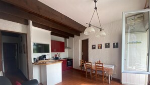 Una sala acogedora con un sofá, una mesa de comedor con sillas, una cocina con armarios rojos y un ventanal grande.