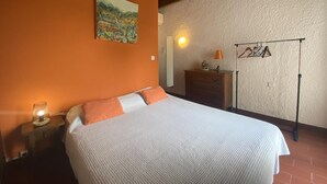 Un dormitorio con cama, mesita de noche, cómoda, lámpara, perchero y un cuadro en la pared.