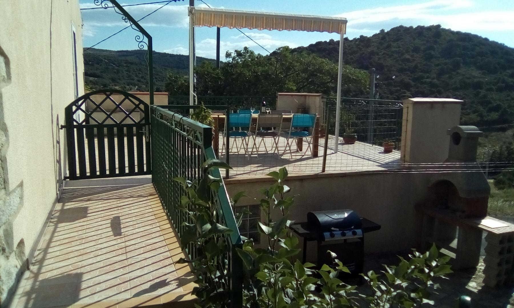 A rooftop terrace with a grill, chairs, and a table.