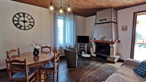 Un salon chaleureux avec un plafond en bois, une table à manger avec des chaises, un téléviseur et une cheminée.