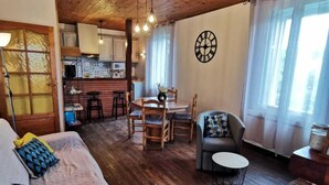 Une pièce chaleureuse avec un plafond en bois, un coin repas comprenant une table et des chaises, un canapé avec des coussins et une petite table ronde.