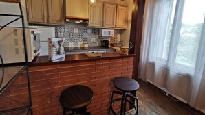 Une cuisine avec un îlot central en briques, un plafond en bois et une fenêtre agrémentée de rideaux.