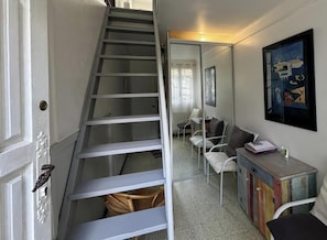 Eine Treppe führt zu einer zweiten Etage, an der Wand ein Spiegel, ein Sofa, ein kleiner Tisch und ein bunter Schrank.