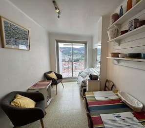 Una habitación acogedora con cama, sillón, mesa y balcón con vistas a la ciudad.