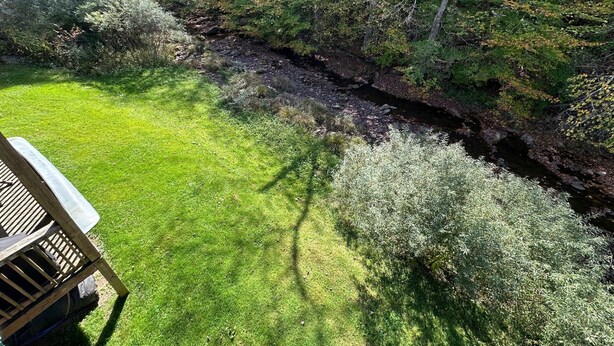 Un espace verdoyant avec une terrasse en bois et un ruisseau.