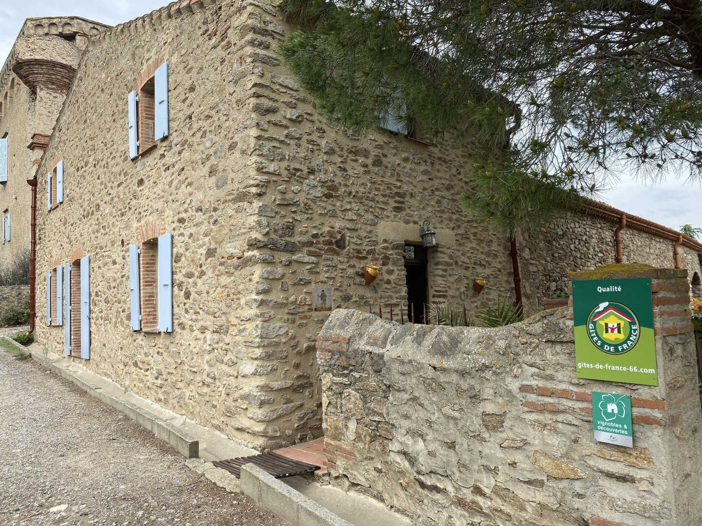 Un edificio de piedra con aspecto rústico, que presenta una pequeña entrada y un cartel que indica que forma parte de la red Gîtes de France.