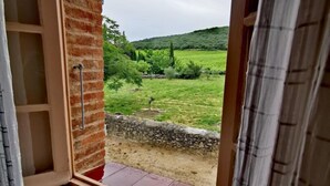 Una ventana con vistas a un paisaje verde, un muro de ladrillo y un muro de piedra.