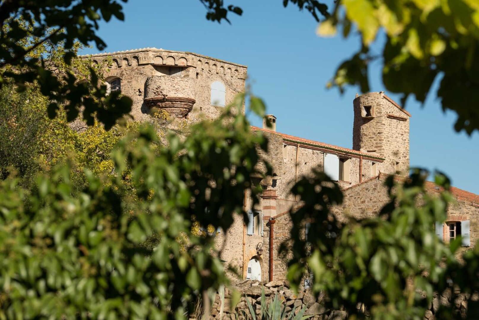 Un edificio histórico de piedra con ventanas de arco y una torre, rodeado de vegetación.